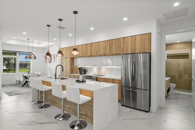 kitchen with a kitchen island with sink, decorative light fixtures, sink, appliances with stainless steel finishes, and white cabinets