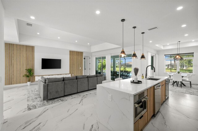 kitchen featuring hanging light fixtures, stainless steel appliances, sink, an island with sink, and a raised ceiling