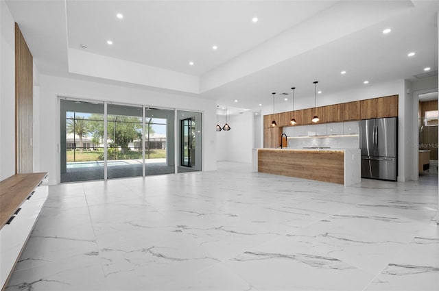 interior space with pendant lighting, a center island, stainless steel refrigerator, and sink