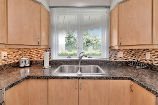 kitchen with dark stone countertops, sink, light brown cabinets, and backsplash