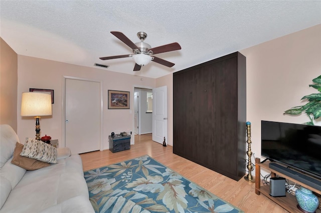 living room featuring ceiling fan, a textured ceiling, and light wood-type flooring