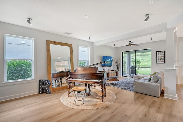 living area with light wood-style floors, baseboards, a healthy amount of sunlight, and ornate columns