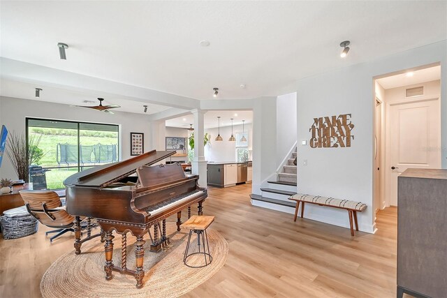 sitting room with light wood finished floors, visible vents, a ceiling fan, ornate columns, and stairs