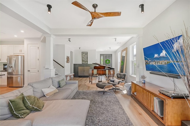 living room featuring light wood-style floors, ceiling fan, decorative columns, and stairway