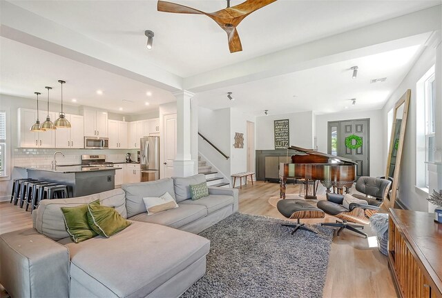 living room featuring light wood finished floors, visible vents, stairs, ornate columns, and recessed lighting