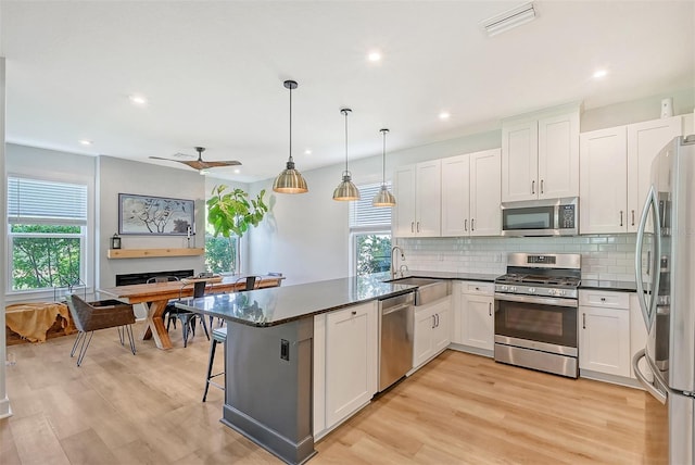 kitchen with tasteful backsplash, white cabinets, appliances with stainless steel finishes, a peninsula, and a sink