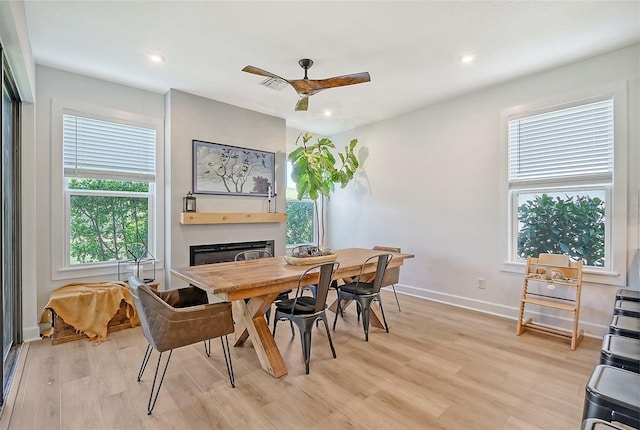 dining space featuring light wood-style floors, a glass covered fireplace, baseboards, and recessed lighting