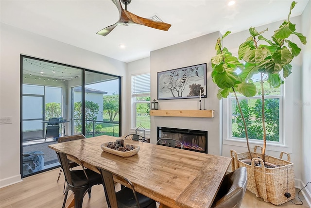 dining area with ceiling fan, plenty of natural light, light wood-style flooring, and a glass covered fireplace