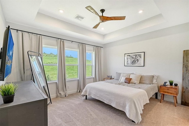 bedroom featuring light carpet, baseboards, visible vents, a ceiling fan, and a tray ceiling