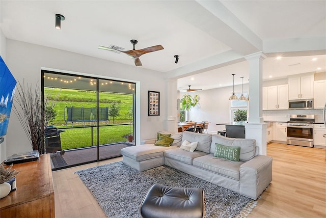 living area with plenty of natural light, ceiling fan, light wood-style flooring, and decorative columns