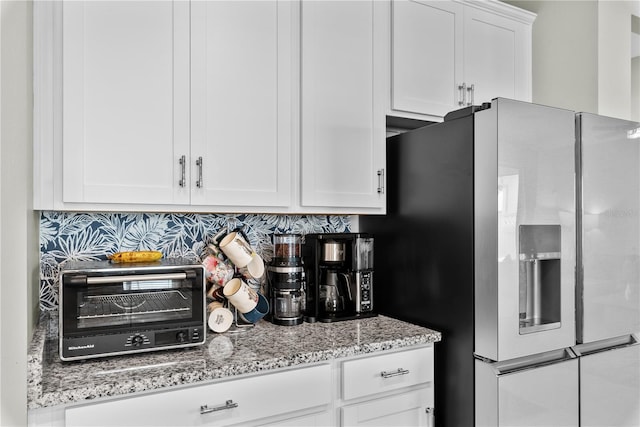 kitchen with light stone counters, white cabinets, stainless steel fridge, and decorative backsplash