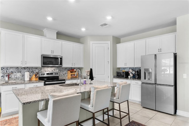 kitchen with white cabinets, an island with sink, appliances with stainless steel finishes, and a kitchen bar