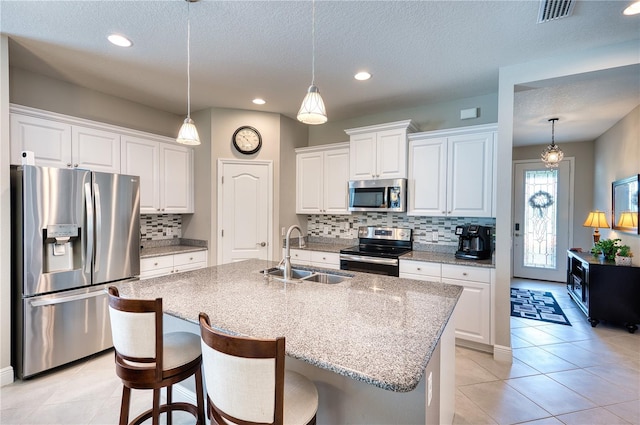 kitchen with decorative light fixtures, appliances with stainless steel finishes, white cabinetry, sink, and an island with sink