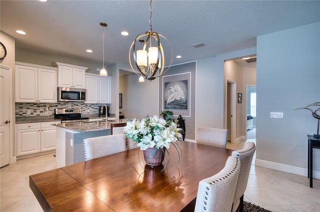 tiled dining area with a textured ceiling, an inviting chandelier, and sink