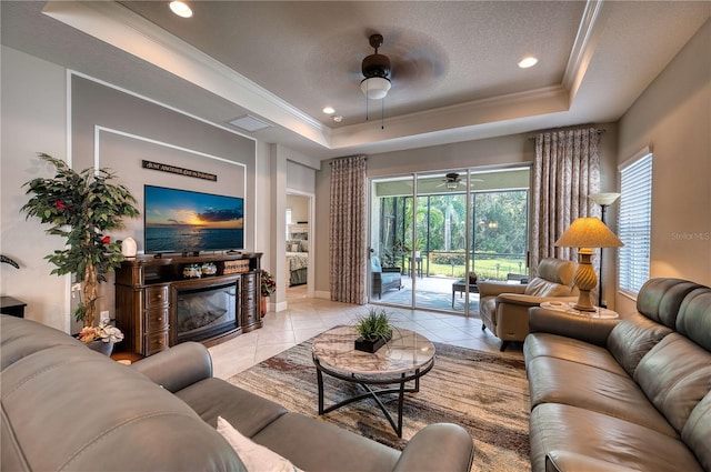 living room with a textured ceiling, light tile patterned floors, a tray ceiling, crown molding, and ceiling fan