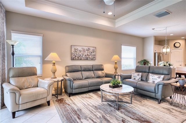 living room with crown molding, ceiling fan with notable chandelier, light tile patterned floors, and a tray ceiling