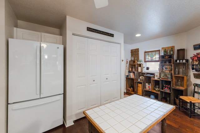 kitchen featuring white cabinetry, tile counters, dark wood-type flooring, a textured ceiling, and white refrigerator