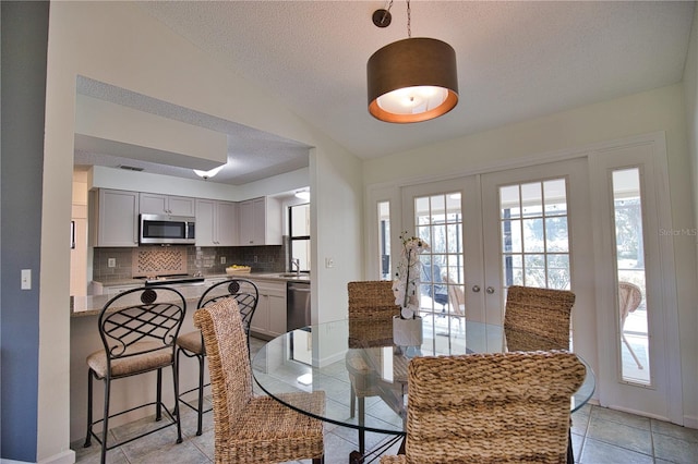 tiled dining room with a textured ceiling, vaulted ceiling, sink, and french doors