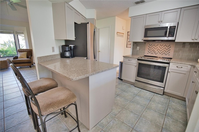 kitchen featuring appliances with stainless steel finishes, light stone counters, kitchen peninsula, a kitchen bar, and ceiling fan