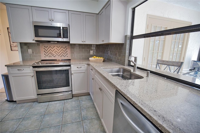 kitchen featuring gray cabinetry, decorative backsplash, light tile patterned floors, stainless steel appliances, and sink