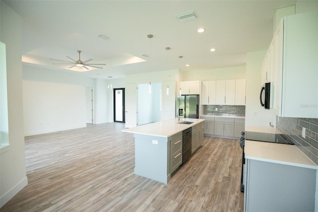 kitchen with backsplash, hanging light fixtures, light hardwood / wood-style flooring, ceiling fan, and a kitchen island with sink