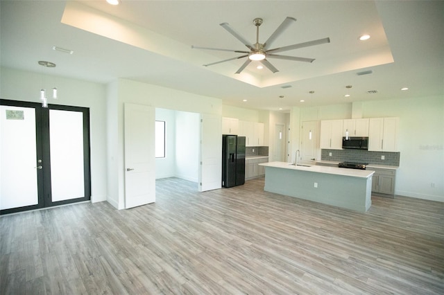 kitchen with appliances with stainless steel finishes, sink, a tray ceiling, an island with sink, and ceiling fan