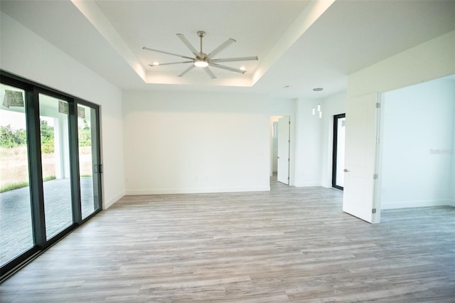 spare room featuring a raised ceiling, ceiling fan, and light hardwood / wood-style floors