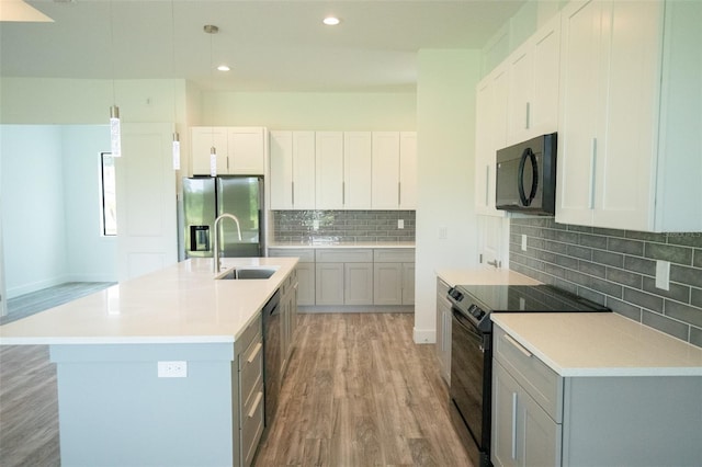 kitchen featuring stainless steel fridge, wood-type flooring, a kitchen island with sink, electric range oven, and sink