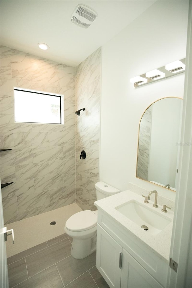 bathroom with tiled shower, vanity, and toilet