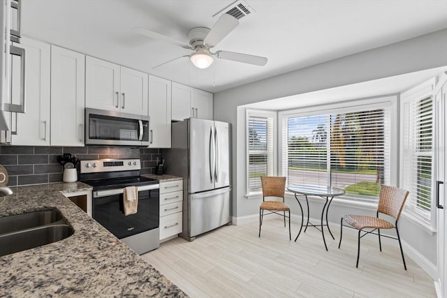 kitchen with white cabinets, a healthy amount of sunlight, tasteful backsplash, light stone counters, and stainless steel appliances