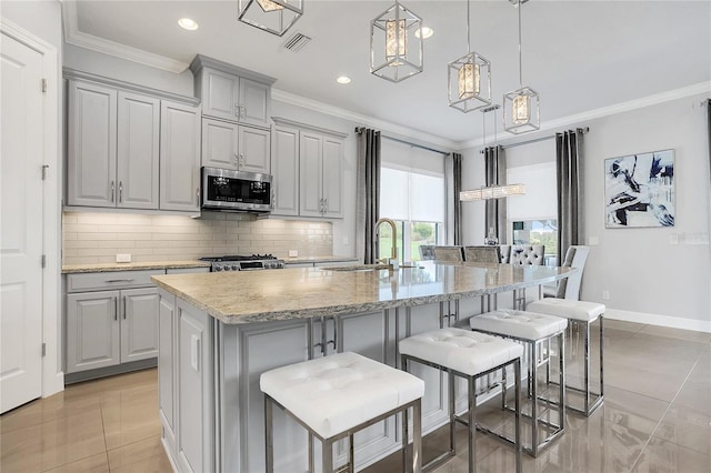 kitchen with hanging light fixtures, appliances with stainless steel finishes, gray cabinets, a kitchen island with sink, and a breakfast bar