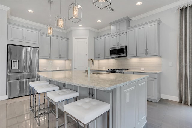 kitchen featuring appliances with stainless steel finishes, a kitchen island with sink, a kitchen bar, sink, and light tile patterned flooring