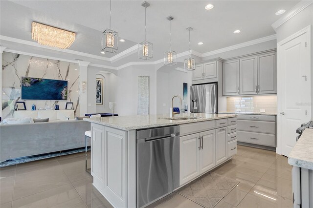 kitchen with decorative light fixtures, appliances with stainless steel finishes, light stone counters, sink, and an island with sink