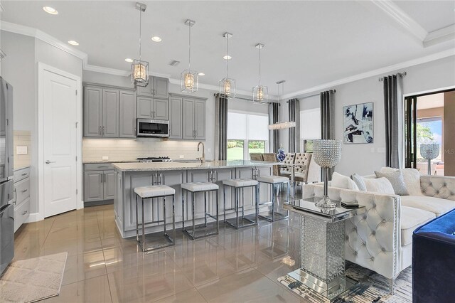 kitchen featuring crown molding, pendant lighting, gray cabinets, and a kitchen island with sink