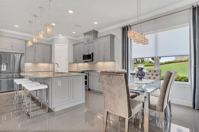 kitchen featuring an island with sink, stainless steel appliances, gray cabinetry, and decorative light fixtures