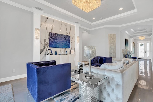 tiled living room featuring a tray ceiling, decorative columns, a notable chandelier, and ornamental molding