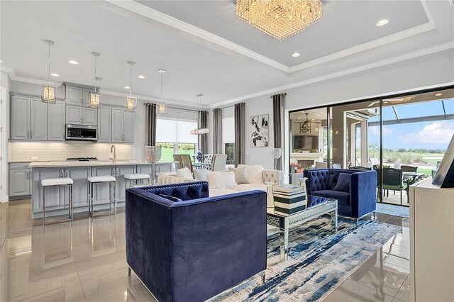 living room featuring sink, a tray ceiling, an inviting chandelier, and ornamental molding