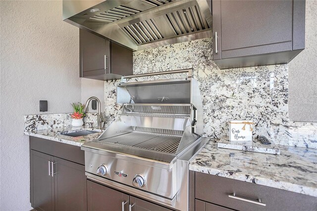 kitchen featuring range hood, light stone counters, and sink