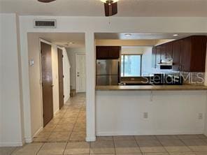 kitchen with light tile patterned floors, stainless steel fridge, kitchen peninsula, ceiling fan, and dark brown cabinetry