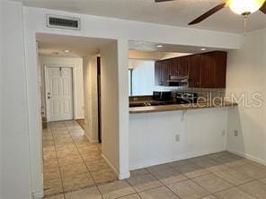 kitchen with dark brown cabinets, kitchen peninsula, ceiling fan, a breakfast bar, and light tile patterned flooring