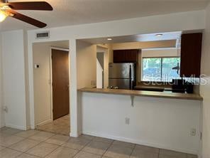 kitchen featuring light tile patterned floors, kitchen peninsula, stainless steel refrigerator, ceiling fan, and dark brown cabinetry