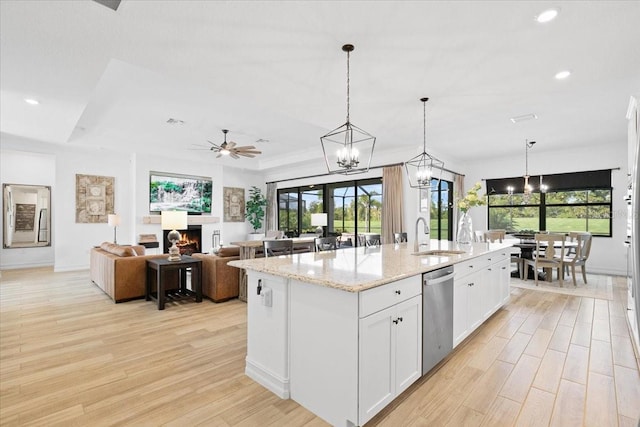 kitchen featuring a tray ceiling, ceiling fan, pendant lighting, white cabinets, and an island with sink