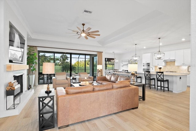 living room featuring light hardwood / wood-style floors, crown molding, ceiling fan, and a tray ceiling