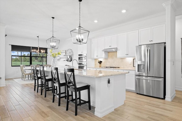 kitchen featuring appliances with stainless steel finishes, a center island with sink, white cabinetry, and hanging light fixtures