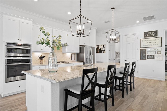 kitchen featuring white cabinetry, hanging light fixtures, a kitchen breakfast bar, a center island with sink, and appliances with stainless steel finishes