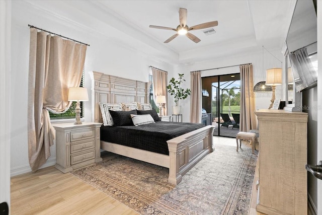 bedroom featuring access to outside, ceiling fan, a tray ceiling, and light hardwood / wood-style floors