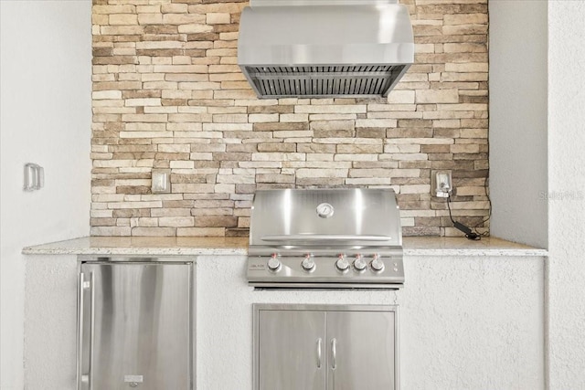 kitchen with light stone counters, wall chimney exhaust hood, and fridge