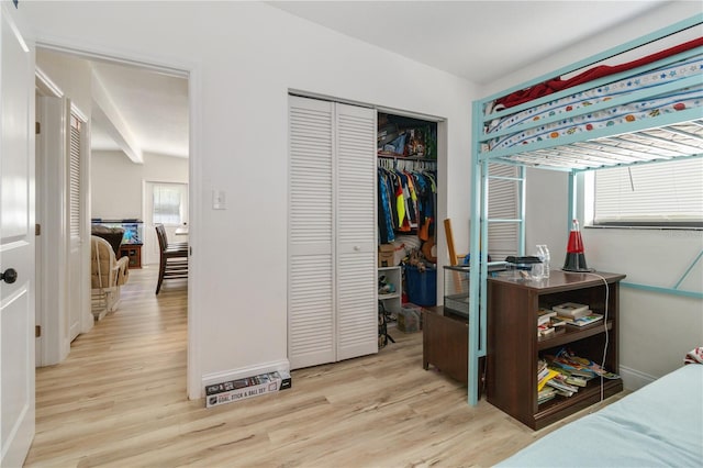 bedroom with beamed ceiling, a closet, and light wood-type flooring