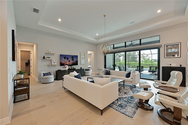 living room with a raised ceiling, light hardwood / wood-style flooring, and an inviting chandelier