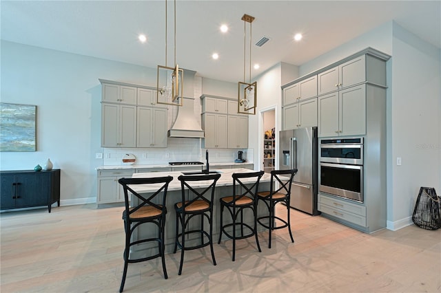 kitchen with light hardwood / wood-style floors, decorative light fixtures, gray cabinets, a kitchen island with sink, and appliances with stainless steel finishes